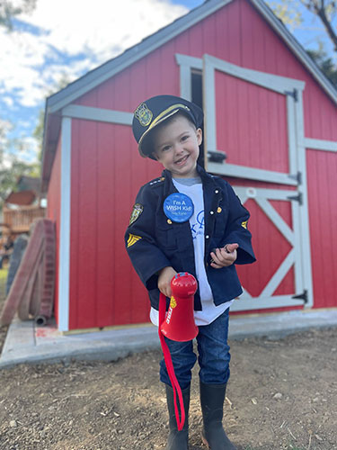 Wish kid dressed as a firefighter by his new playhouse