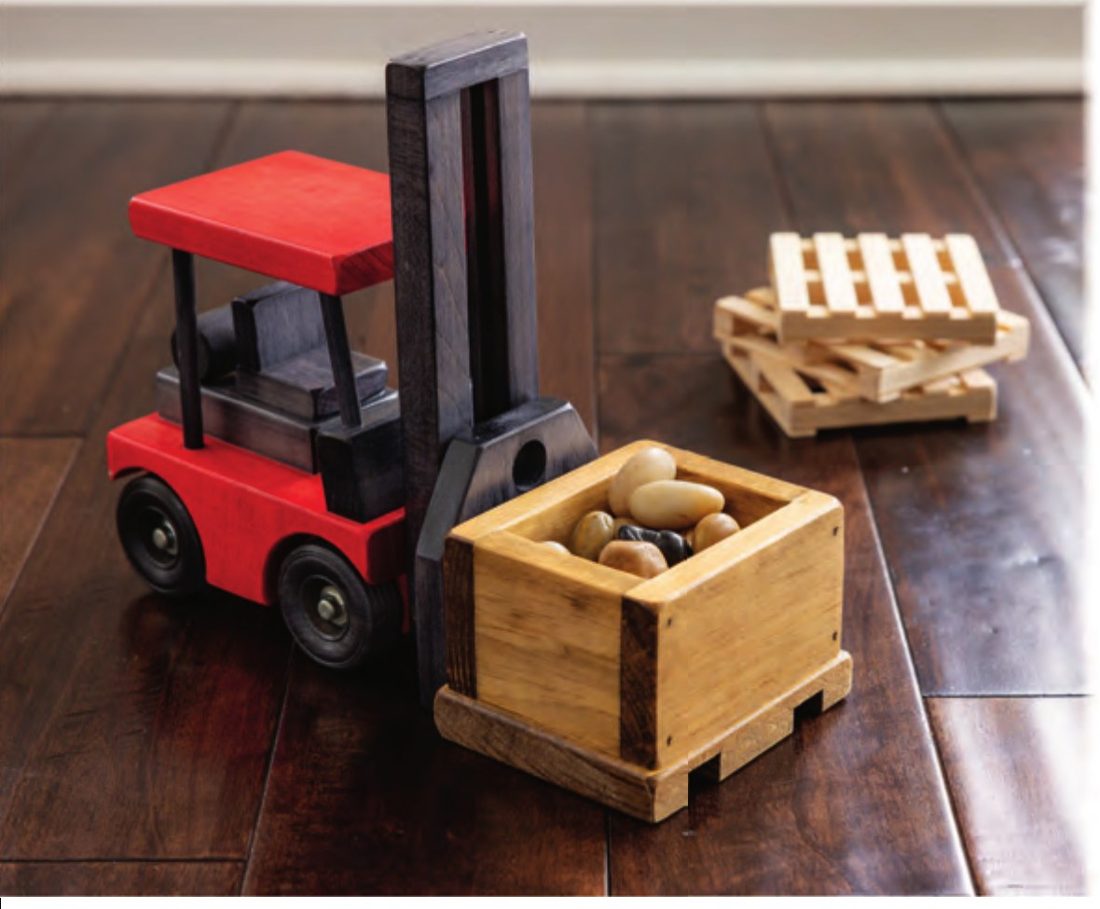 Red wooden fork lift carrying a crate on a pallet, with stacked pallets behind